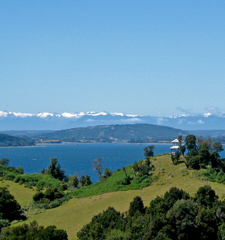 Gr&uuml;ne H&uuml;gel und der Blick &uuml;bers Meer auf die endlose wei&szlig;e Kette der Anden im Norden Patagoniens: das ist die Insel Chilo&eacute; bei klarem Wetter. 