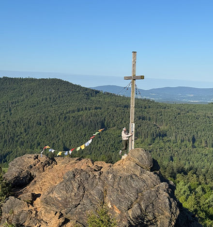 Lina aus dem Bergzeit Team genießt den Ausblick am Gipfelkreuz des Silberberges.