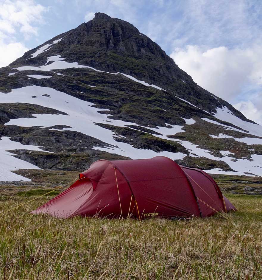 rotes Zelt steht auf Wiese vor Berg mit Schneefeldern